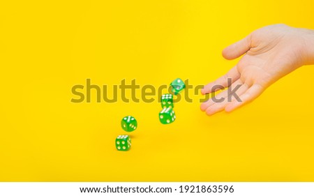 A lot of green dice fall from the hand on a yellow background with space for text: board games, selective focus on the hand, a photo in motion