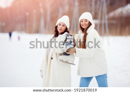 Young happy women in winter with skates on open air ice rink. Girl friendship concept.
