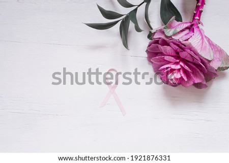 Pink ribbon on a white wooden background with flowers.