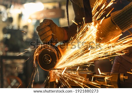 Locksmith in special clothes and goggles works in production. Metal processing with angle grinder. Sparks in metalworking. Royalty-Free Stock Photo #1921880273