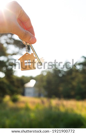 Wooden pendant of a house and key. Background of countryside, nature. Dream of home, building, delivery of the project, moving to a new house, mortgage, rent and purchase real estate. Copy space