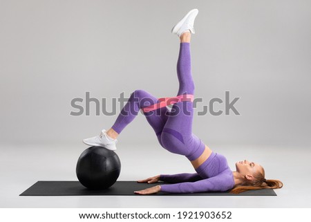 Fitness woman doing glute bridge exercise with resistance band on gray background. Athletic girl working out Royalty-Free Stock Photo #1921903652