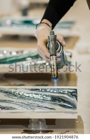 a female hand in a glove holds a manual gas burner, creating a beautiful painting using resin art technique