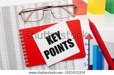 Gold-rimmed glasses, a red pen, color tables and a red notebook with a white card with the text KEY POINTS on the desktop. Business concept. View from above