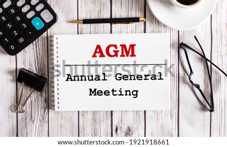 AGM Annual General Meeting is written in a white notepad near a calculator, coffee, glasses and a pen. Business concept Royalty-Free Stock Photo #1921918661