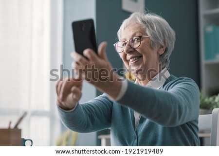 Happy senior woman using her smartphone, she is taking selfies and sharing online