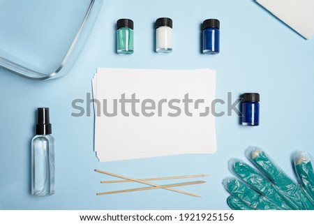 Artist workspace with paper shirts, glass dish with water, colors, graves on blue paper background. High quality photo