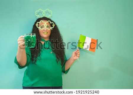 Woman celebrating St. Patrick´s Day with luminous shamrock glasses and headband, green beer mug and irish flag. With green background.