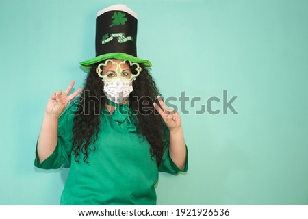 Woman with hat and luminous shamrock glasses and mask by Covid 19 celebrating St. Patrick´s Day. With green background.