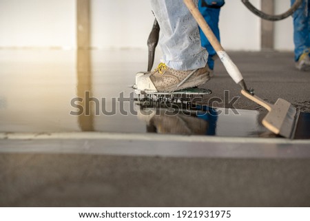 Worker working on the floor of an industrial building. Construction worker producing grout and finishing wet concrete floor.
