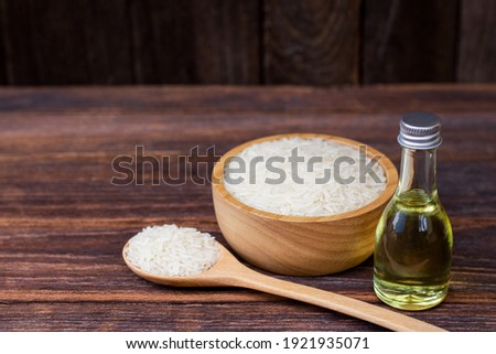Rice bran oil extract in glass bottle and white rice in wooden bowl and spoon isolated on wooden table background. Selective focus. Royalty-Free Stock Photo #1921935071