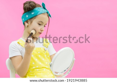 Littttle girl posing for a photo with make up brush looking in the mirror.