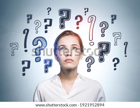 European attractive young woman in white shirt looking up and pondering about career opportunities. Question marks drawn on wall behind. Concept of searching for an answer. Royalty-Free Stock Photo #1921952894
