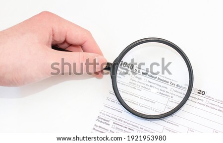 Closeup photograph of the 1040 federal government individual income tax return form in a white envelope with a man holding a magnifying glass over the text to enlarge it.