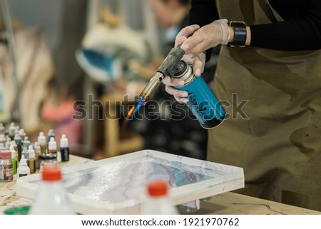 at the workshop, sealed hands work with a gas burner, creating a picture of resin
