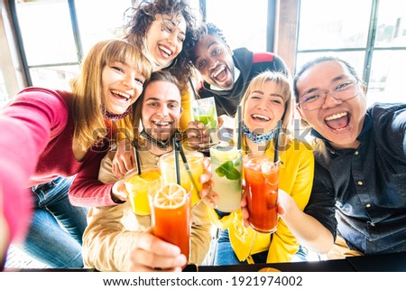 Multiracial people wearing protective face masks drinking cocktails at bar restaurant - New normal friendship concept with young friends taking a selfie - Food, drink and people concept. Royalty-Free Stock Photo #1921974002
