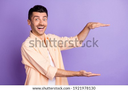 Photo of excited young guy palms measure empty space wear beige shirt isolated purple color background
