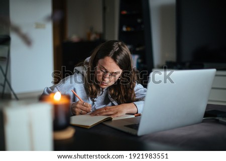 Young woman sit alone in cosy living room of authentic home, make notes on information she finds online. Internet for learning and job search. Work from home concept. Millennial lifestyle Royalty-Free Stock Photo #1921983551