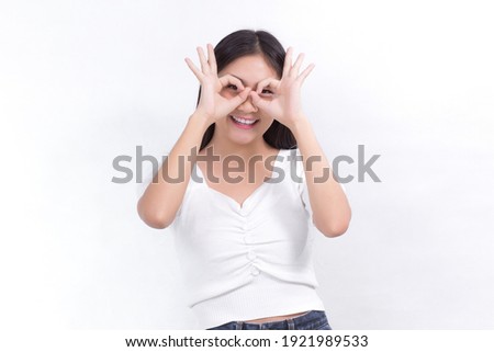Asian female with long black hair wears white shirt and shows hand “okey” sign on white background.