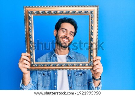 Young hispanic man holding empty frame smiling with a happy and cool smile on face. showing teeth. 