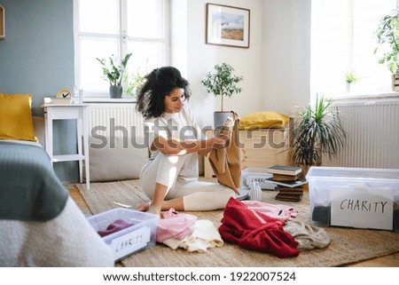 Young woman sorting wardrobe indoors at home, charity donation concept. Royalty-Free Stock Photo #1922007524