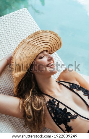 Gleesfully laughing by baring the beautiful teeth of a girl in a hat and swimsuit at the pool in a schizlong close-up. High quality photo