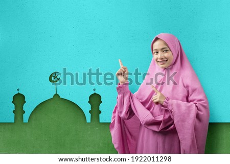 Asian Muslim woman in a veil pointing something with mosque background. Empty area for copy space