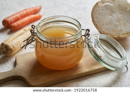 Bone broth in a glass jar on a white background, with vegetables