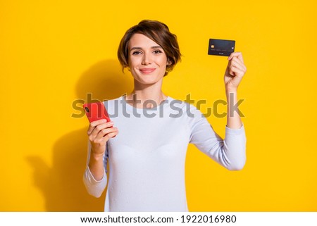 Photo portrait of woman showing card holding phone in one hand isolated on bright yellow colored background