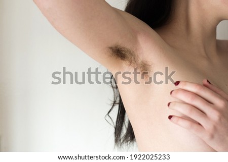 Beautiful female armpits with dark hair. Woman raising her arm and showing unshaven hairy armpits. Bodypositive, feminism and body care concept.