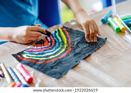 Closeup of child painting rainbow picture with different stick colors on black background during pandemic coronavirus quarantine disease. Children paint rainbows around the world.