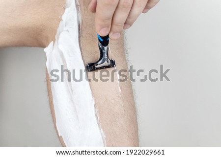 A man on a white background shaves his legs. Hairy legs and care for them. Gender equality concept. A close-up showing the foam, razor, and shaved hair on a smooth leg. Royalty-Free Stock Photo #1922029661