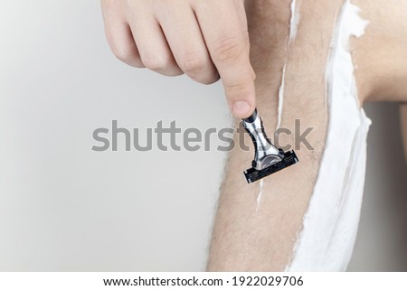 A man on a white background shaves his legs. Hairy legs and care for them. Gender equality concept. A close-up showing the foam, razor, and shaved hair on a smooth leg.