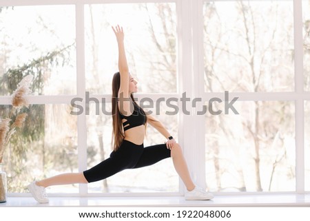 Beautifull brunette woman doing stretching on windowsill at home. Attractive fit girl training at home. Copy space Royalty-Free Stock Photo #1922048006