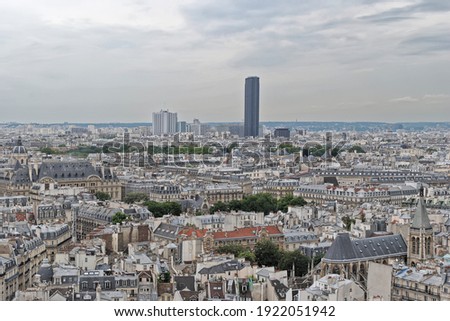 Top view of the rooftops of Paris. In the background, the Montparnasse Tower rises against the gloomy sky.