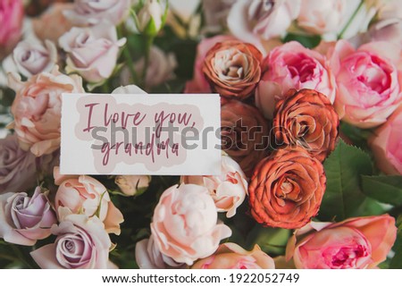 white gift card with the  text inscription I love you grand mother in a bouquet of bright beautiful multi-colored roses, the concept of congratulations on the holiday