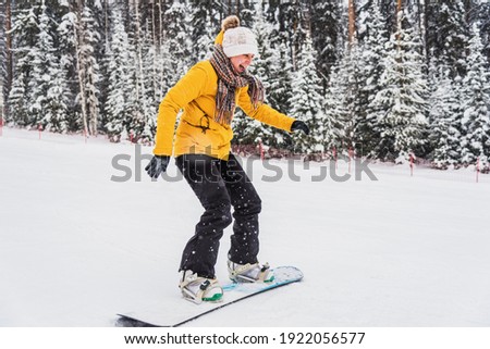 Young joyful woman is rolling on a snowboard down the hill