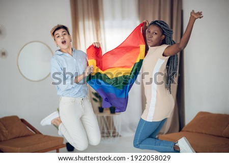 Joyful mood. Two young girls holding a rainbow flag and jumping