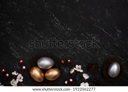 Golden and silver Easter eggs with plum blossom flower on dark black slate table background.