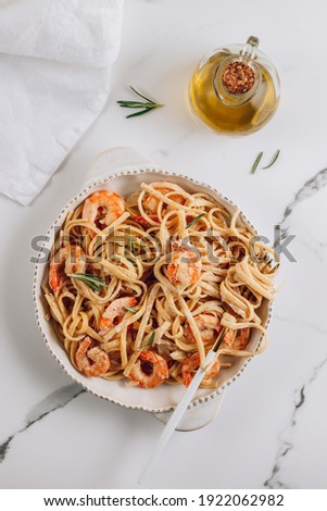 Pasta tagliatelle with shrimps in creamy sauce on white plate over white marble background. Top view