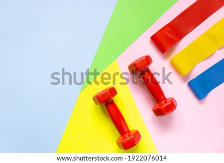 Red weights and rubber bands for sports on a colorful background. The concept of movement, sports, and a healthy lifestyle. Top view, free space for text.