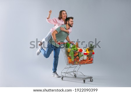 Young couple with shopping cart full of groceries on grey background Royalty-Free Stock Photo #1922090399