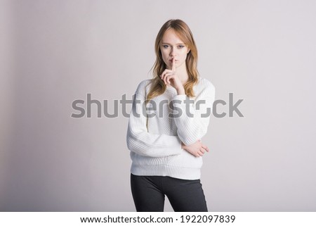 Attractive Caucasian young woman blonde in casual clothes shows gesture of silence isolated on gray studio background. A secret, a chatter, a mystery, a whisper.