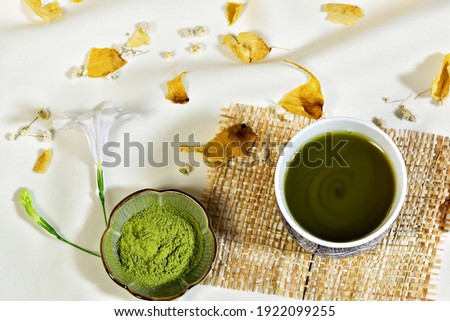 matcha green tea and green tea powder on creamy cloth with fresh flower and dried leaves