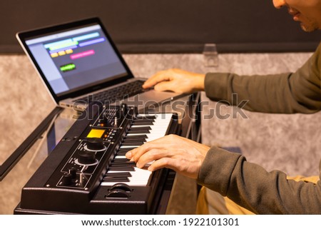 male musician enjoy playing keyboard synthesizer for arranging a song on laptop computer in home studio. music production technology