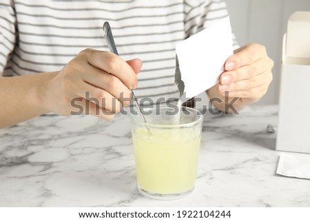 Woman pouring and stirring powder from medicine sachet into glass with water at table, closeup