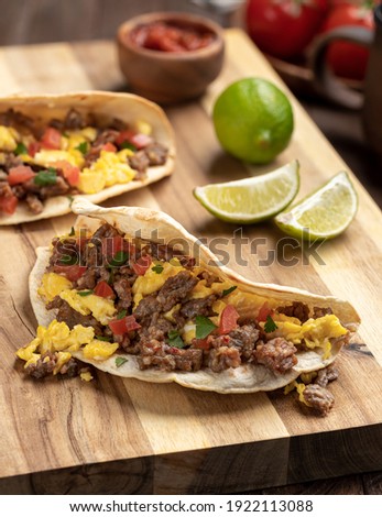 Breakfast tacos with scrambled egg, sausage and tomato on a wooden cutting board