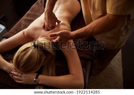 Cropped photo of tranquil woman laying down while receiving a massage from a professional masseur