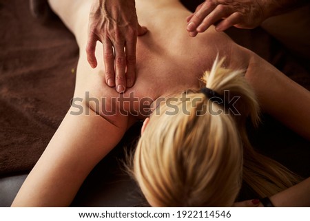 Fragment photo of a shirtless woman having her shoulder blades massaged by a professional