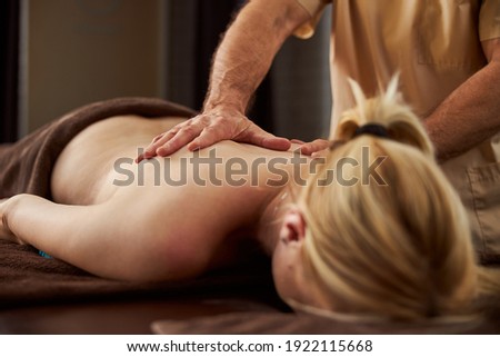 Cropped photo of blonde lady lying with her face down while receiving proper massage from a specialist
